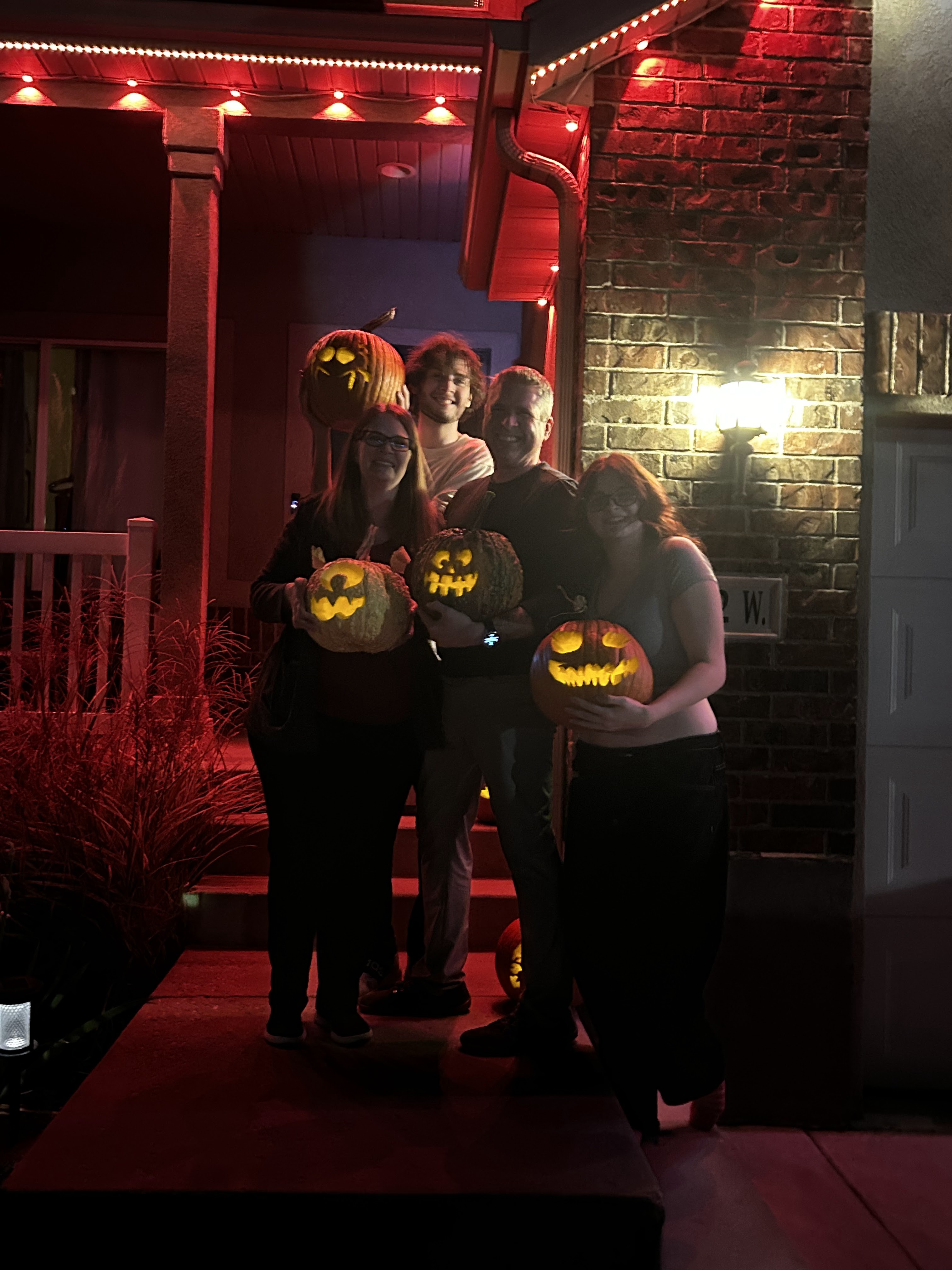 Kyle with family on a porch at night, smiling and holding glowing Halloween jack-o'-lanterns