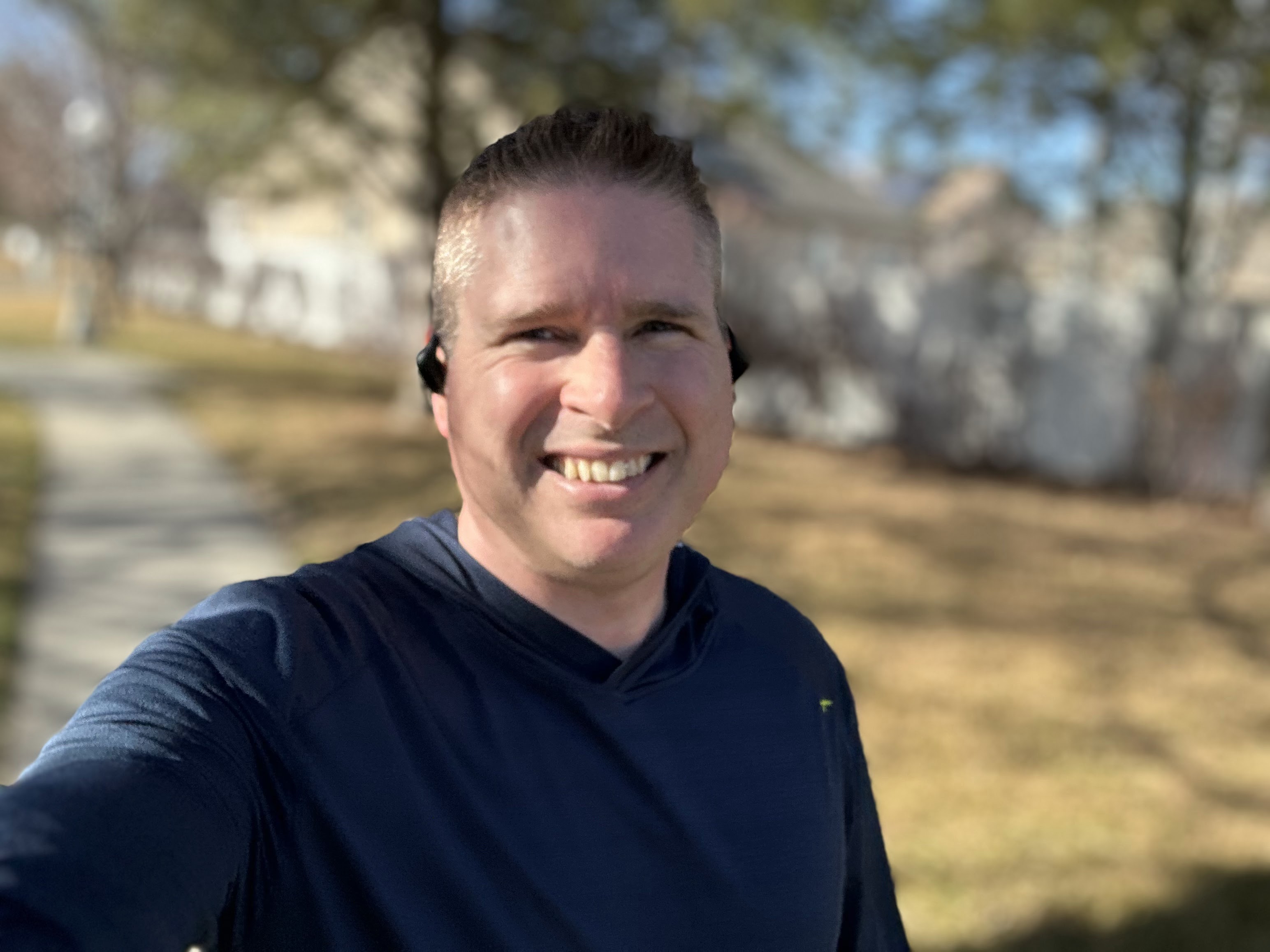 Recent outdoor selfie of Kyle Erb smiling on a sunny day, wearing a navy athletic shirt and headphones