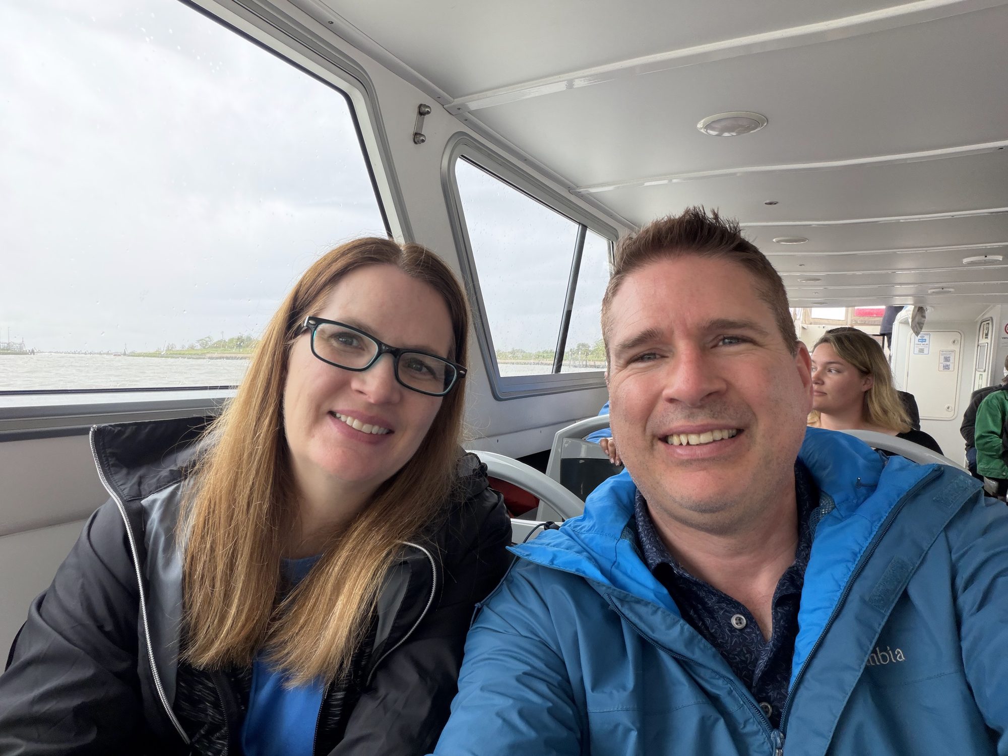 Kyle and Mandy smiling in a passenger boat cabin with water and shoreline visible through the windows