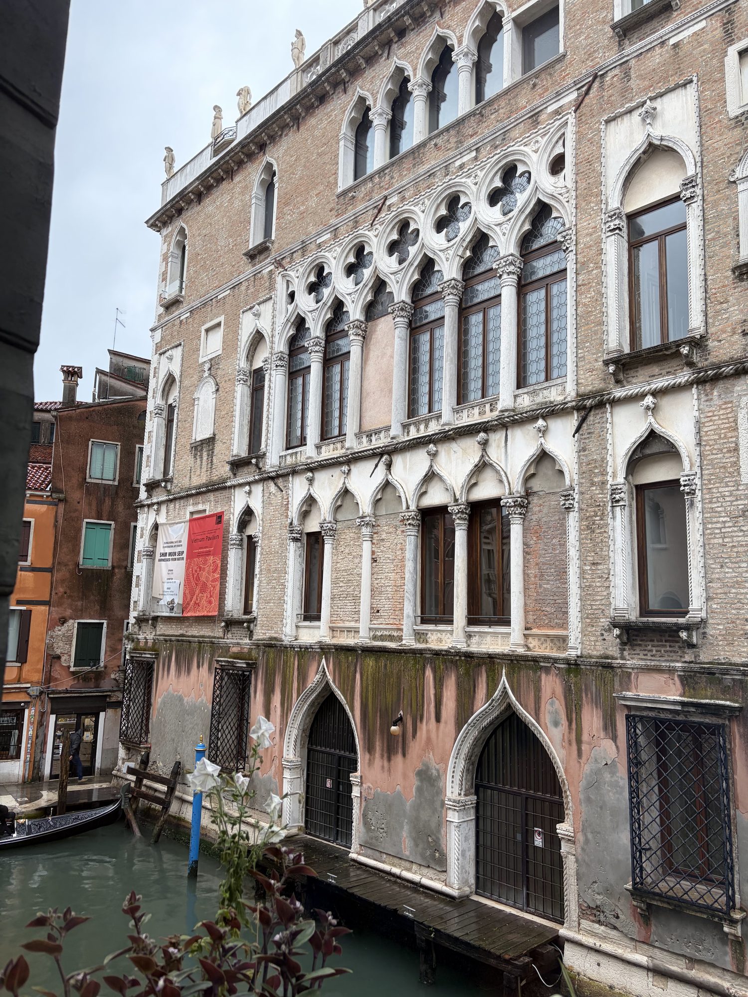 Venetian Gothic canal facade with quatrefoil windows, weathered stone, and a gondola tip in the foreground