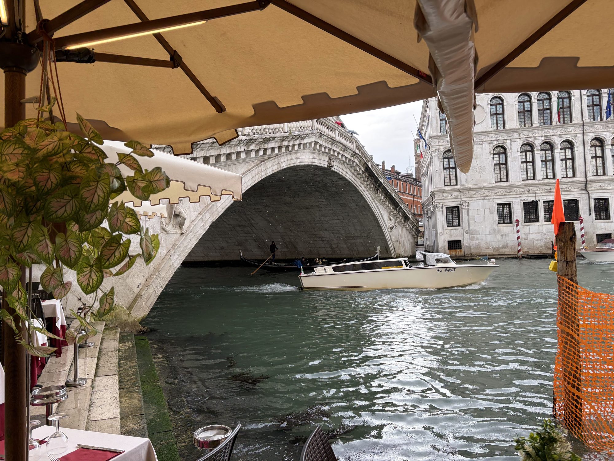 Rialto Bridge across the Grand Canal seen from a canal-side cafe terrace with umbrella and table linen