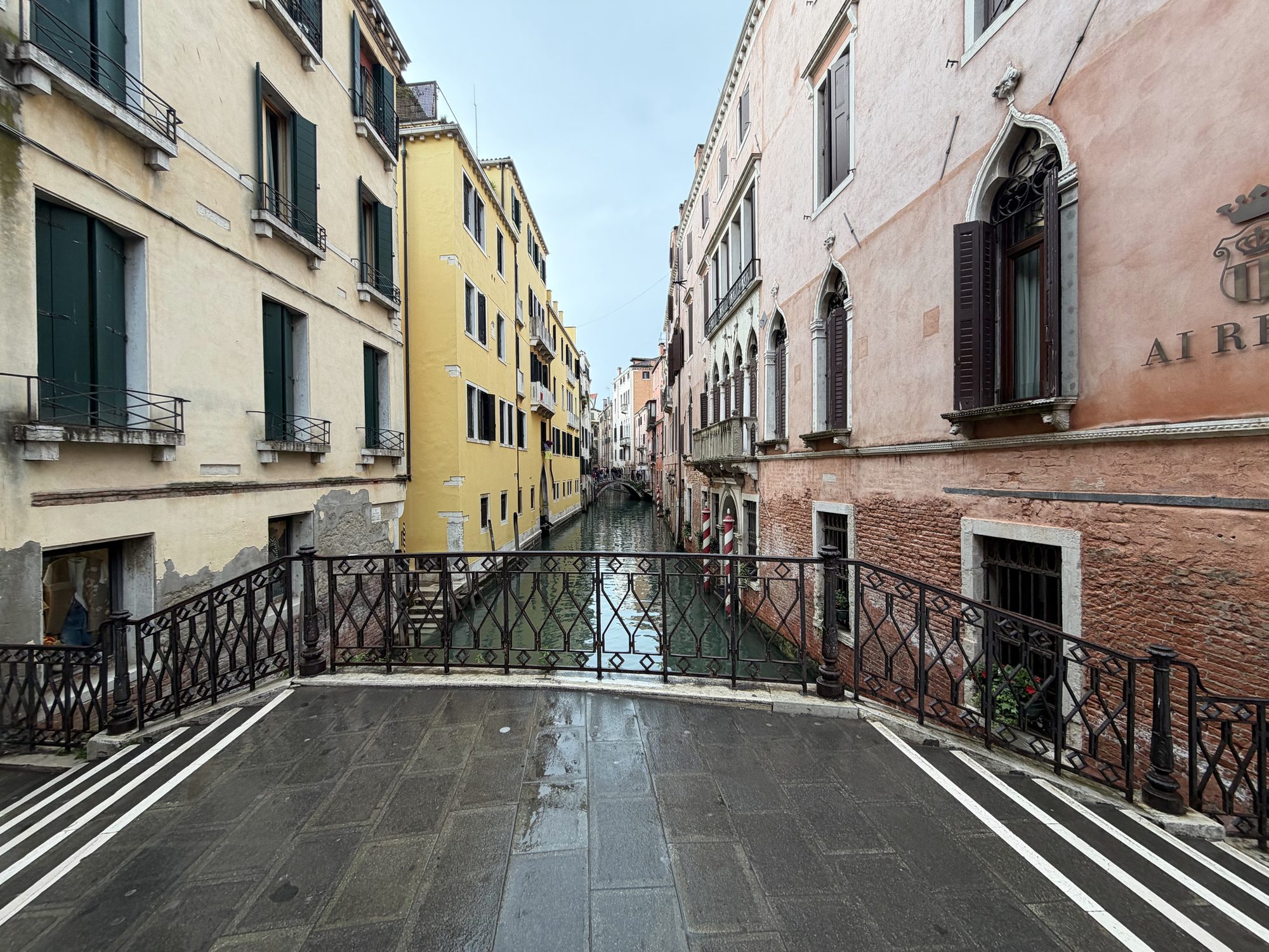 Canal receding between yellow and terracotta Venetian buildings, viewed from a stone bridge railing
