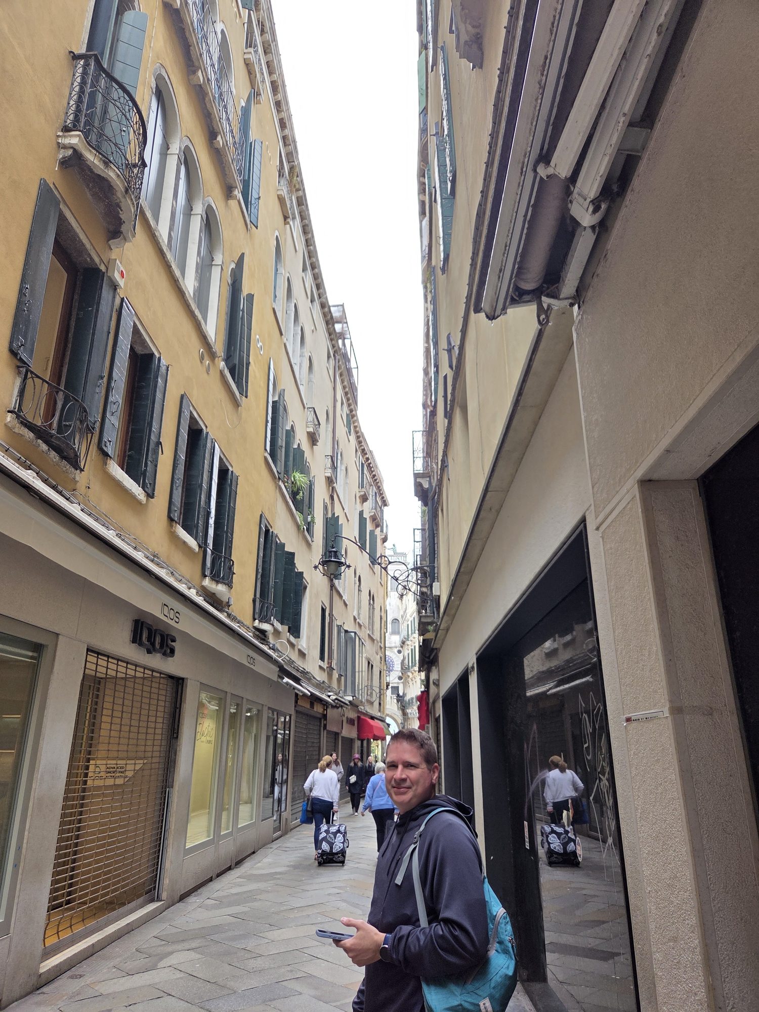Kyle smiling in a narrow Venetian calle lined with yellow buildings and green shutters, backpack on