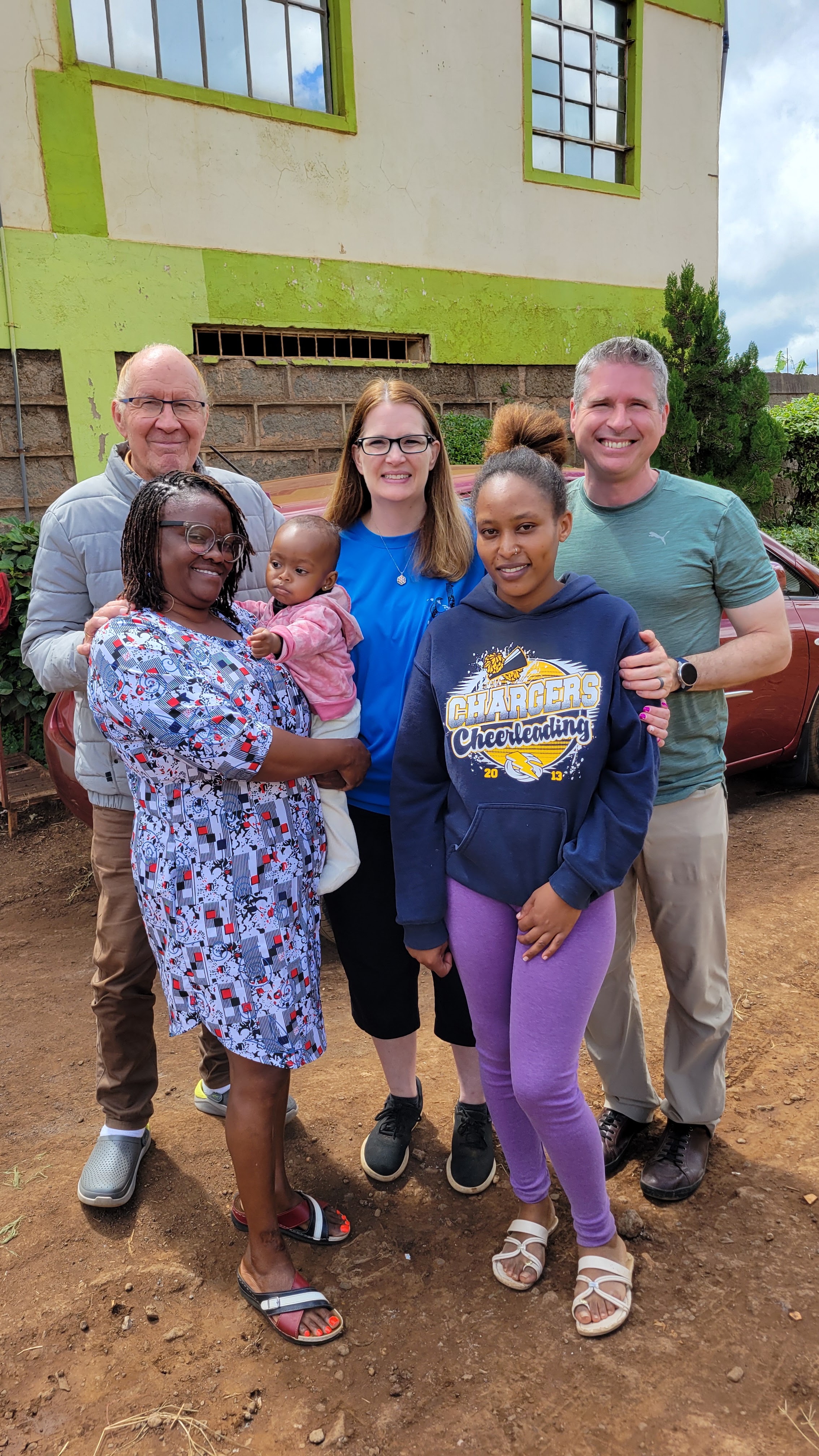 Kyle with friends and family outdoors in Kenya, standing together beside a building