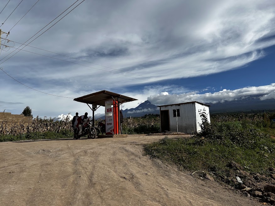 Rural roadside petrol pump and metal shed with a jagged mountain peak rising above clouds in the distance