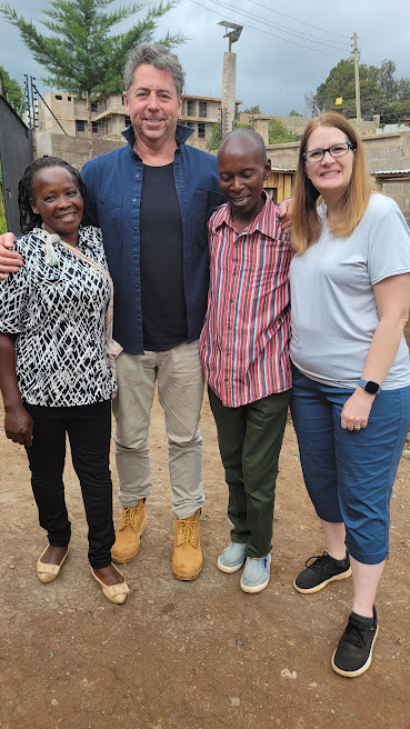 Four adults smiling together outdoors beside a building under construction near the training institute