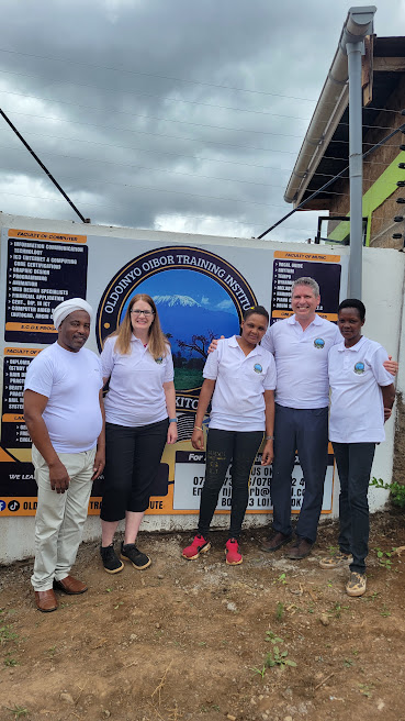 School team and visitors standing together in front of the Oldoinyo Oibor Training Institute sign in Loitokitok