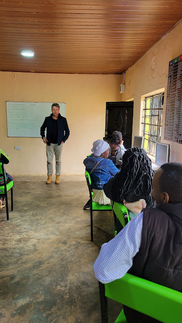 Instructor speaking at the front of a computer classroom at Oldoinyo Oibor Training Institute, with students seated in green chairs