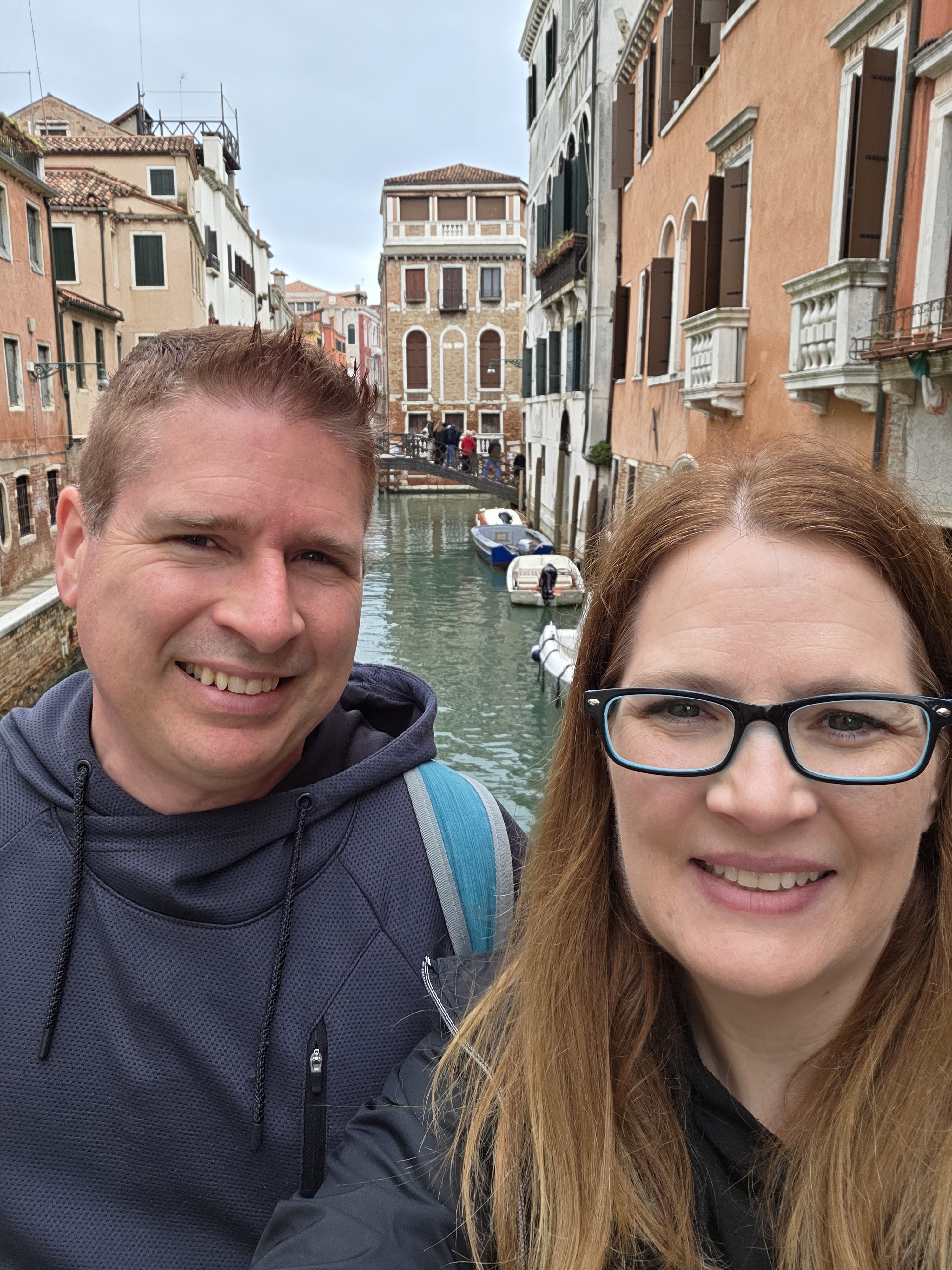 Kyle and Mandy smiling on a bridge over a canal in Venice during an anniversary trip with friends
